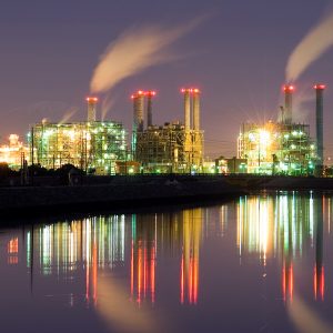 Illuminated power plant at night, its reflection in nearby water