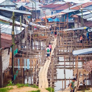 A wooden walkway winds through a slum built over water