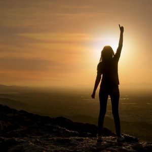 Woman standing on mountain at sunset pointing toward the sky